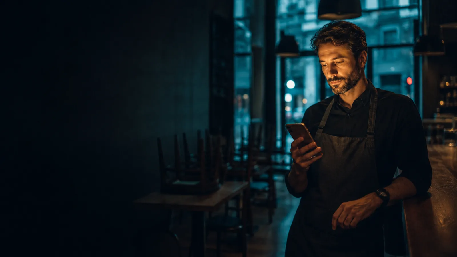 Restaurator wieczorem sprawdza zamówienie w telefonie w zamkniętej restauracji